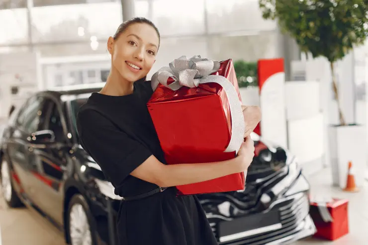 Vendedora en un concesionario de coches con un regalo rojo 